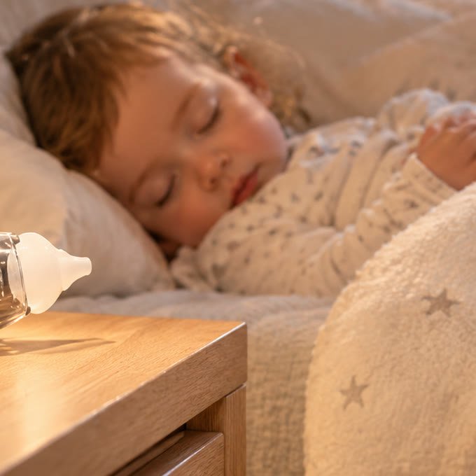 Un enfant dort paisiblement, le mouche bébé Redalis posé sur la table de nuit
